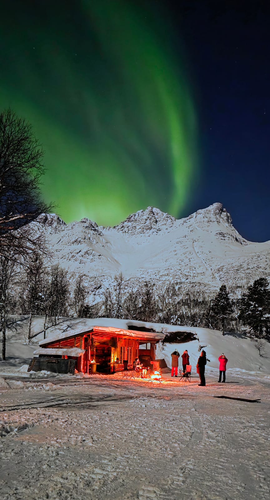 Northern Lights over the cabin and the campfire at the basecamp